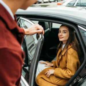 Over shoulder view of taxi driver opening car door for woman