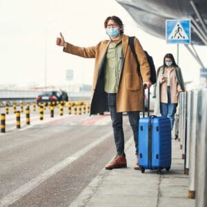 Stylish young man in medical mask catching taxi at airport