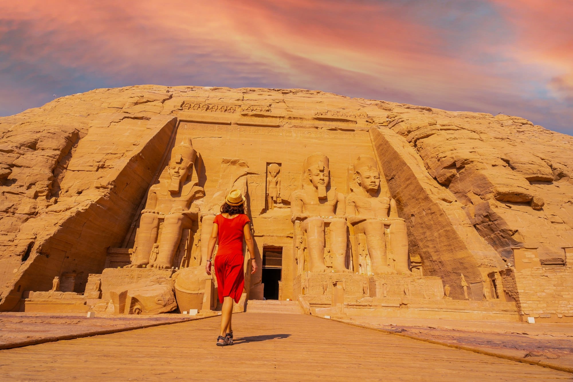 A young tourist girl in red dress walking towards the Abu Simbel Temple